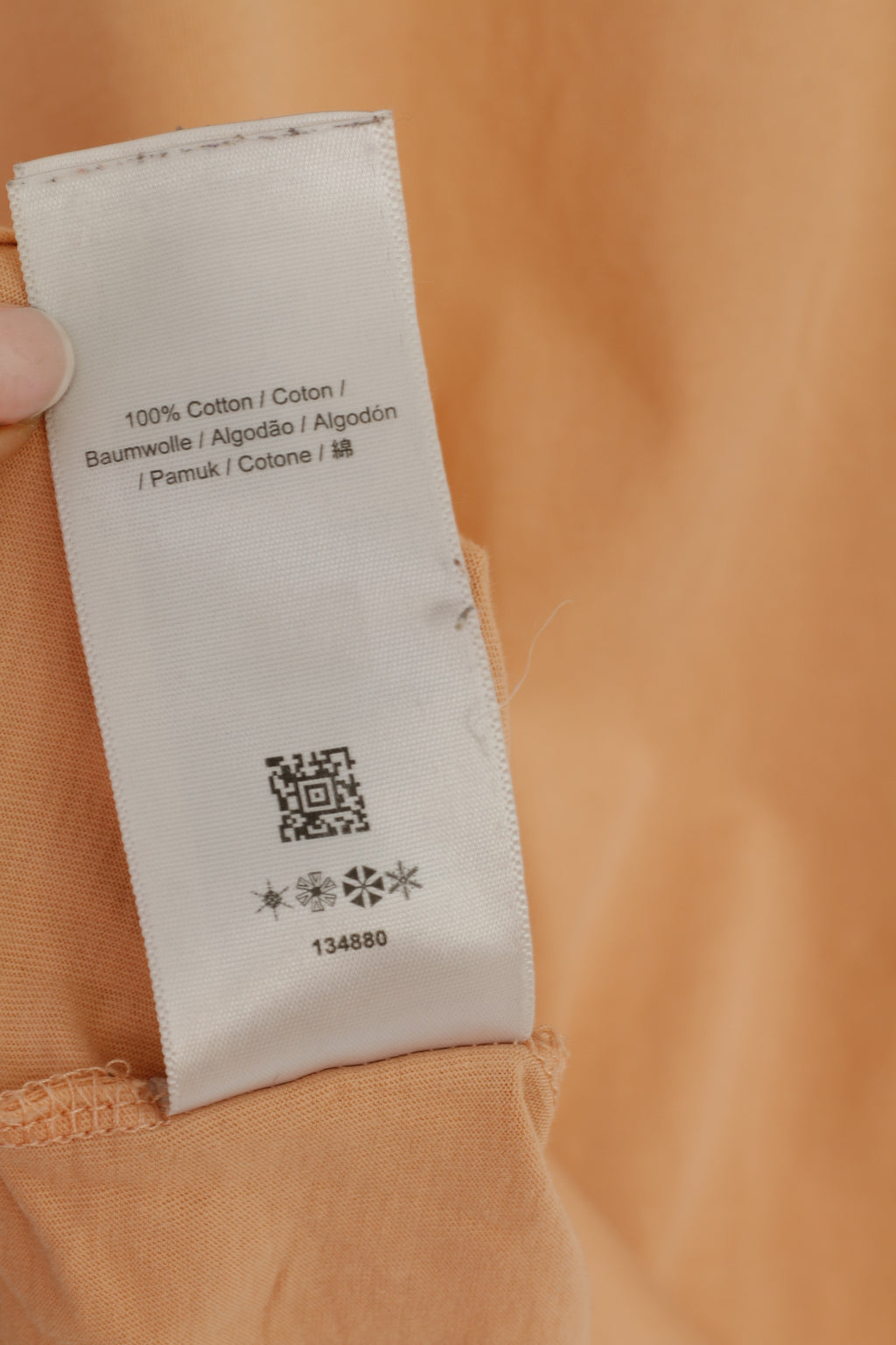 Close-up of a fabric tag on an orange garment with a QR code and text.