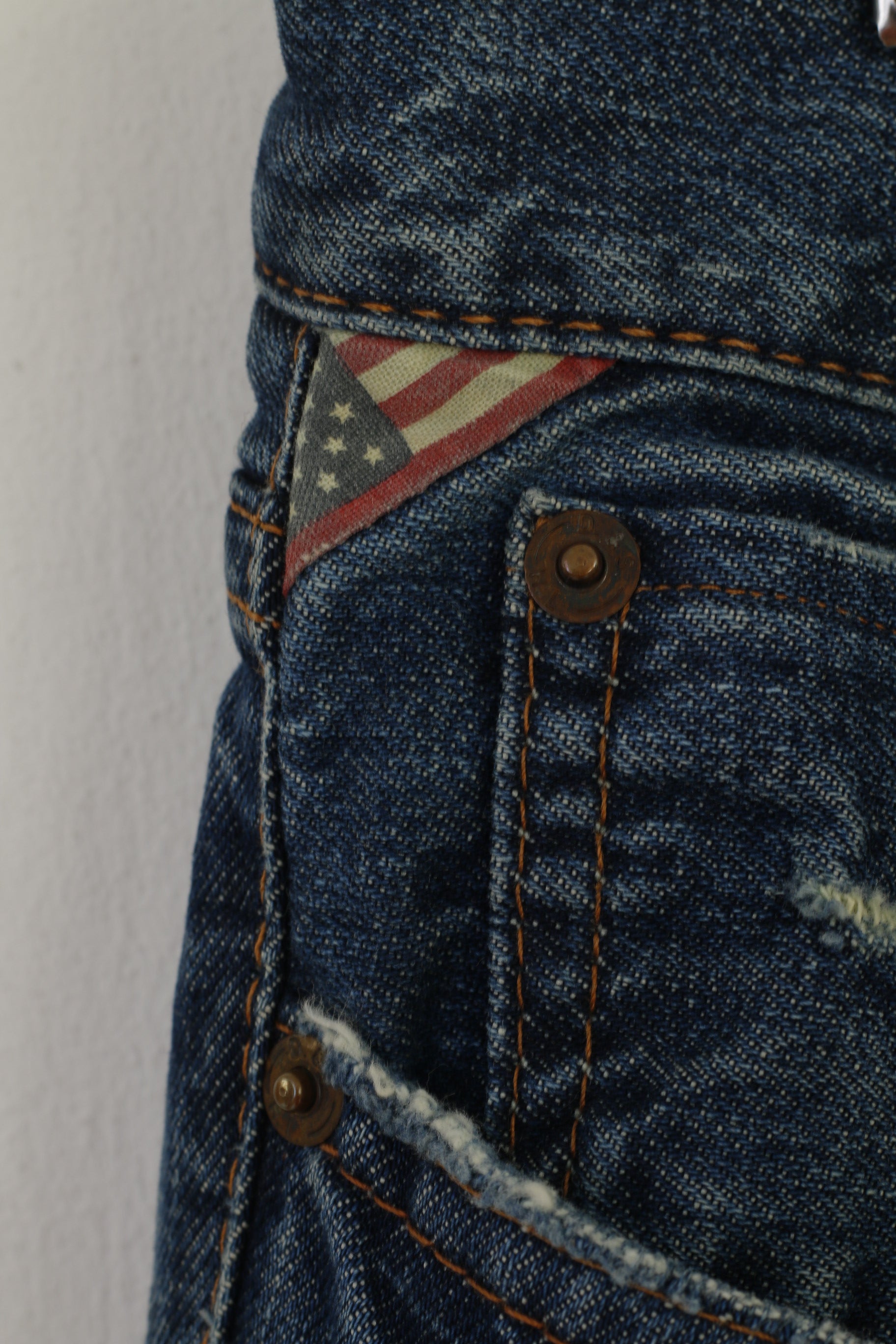 Close-up of blue denim fabric with an American flag patch and stitching details.